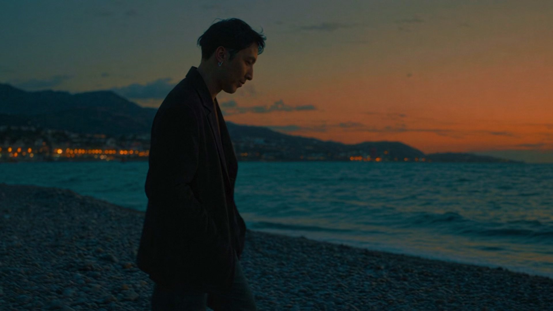 Haddy Elnath beside the sea at dusk, with mountains and an orange sky behind him.